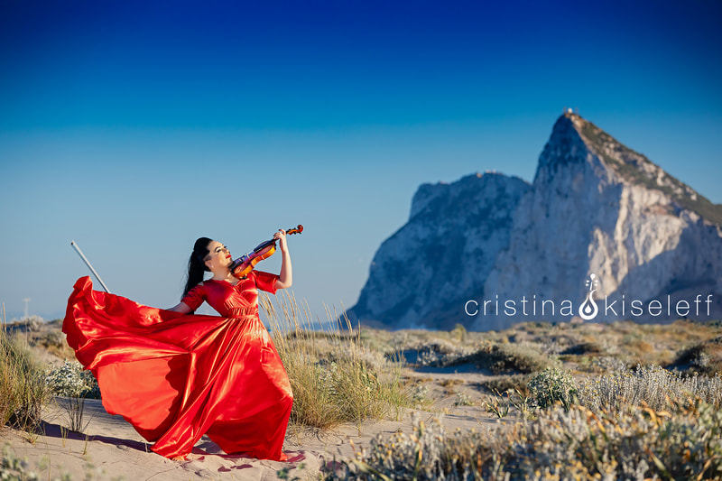 Cristina Kiseleff Electric Violinist performing in front on The Rock of Gibraltar in Spain with a long red dress