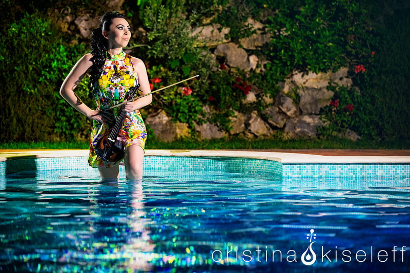 Cristina Kiseleff Electric Violinist standing in a blue pool in Italy wearing a Motivi dress holding a Yamaha electric violin